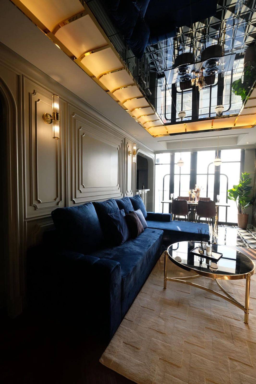 Living room with blue velvet sofa, gold accents, and chic decor elements.