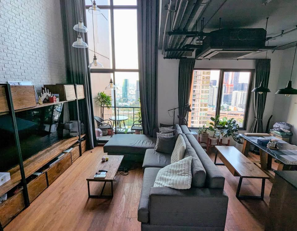 Spacious loft-style 1-bedroom duplex at Villa Asoke with high ceilings, floor-to-ceiling windows, modern furnishings, and city skyline views in Bangkok.